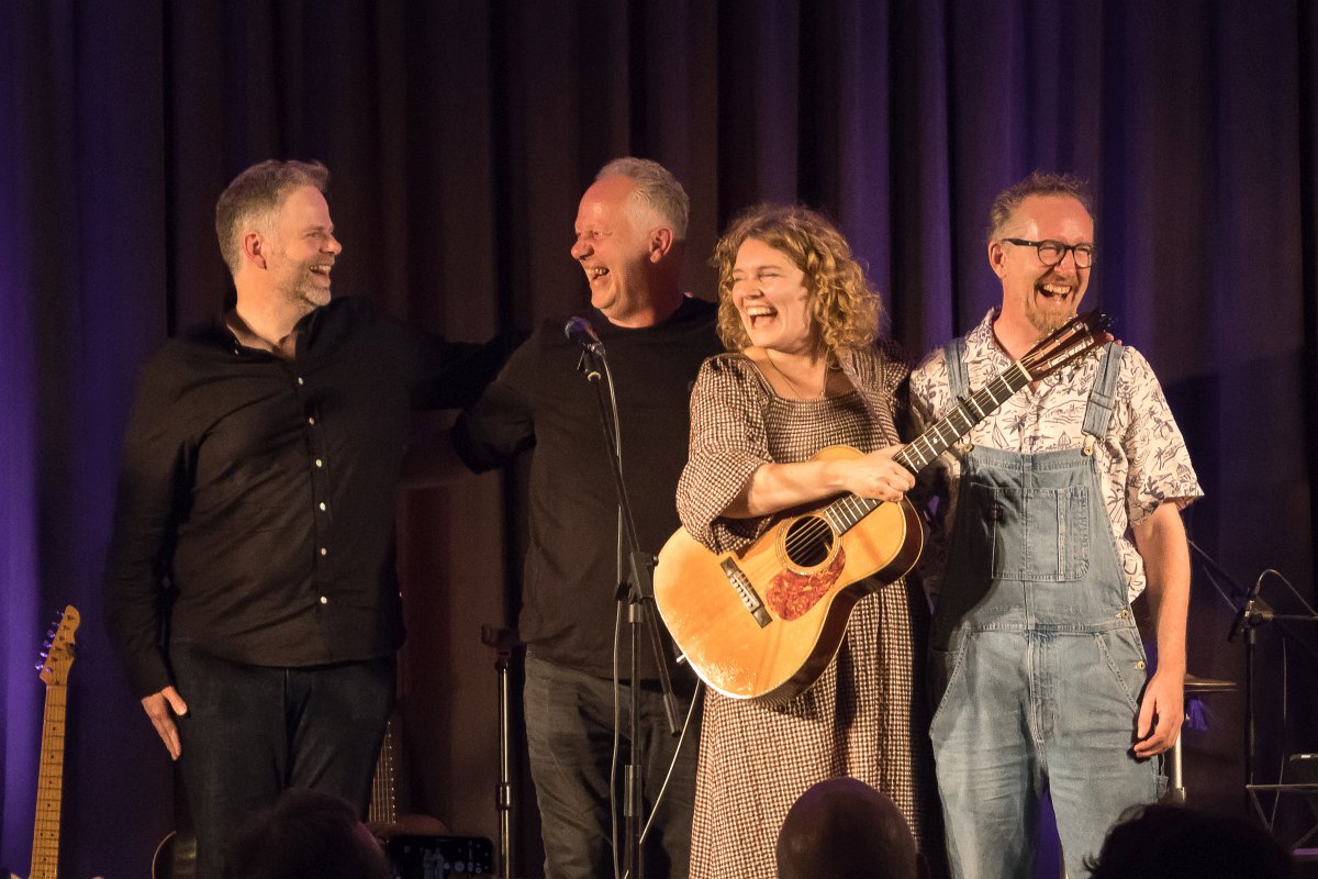 Nina en drie muzikanten lachen samen op het podium