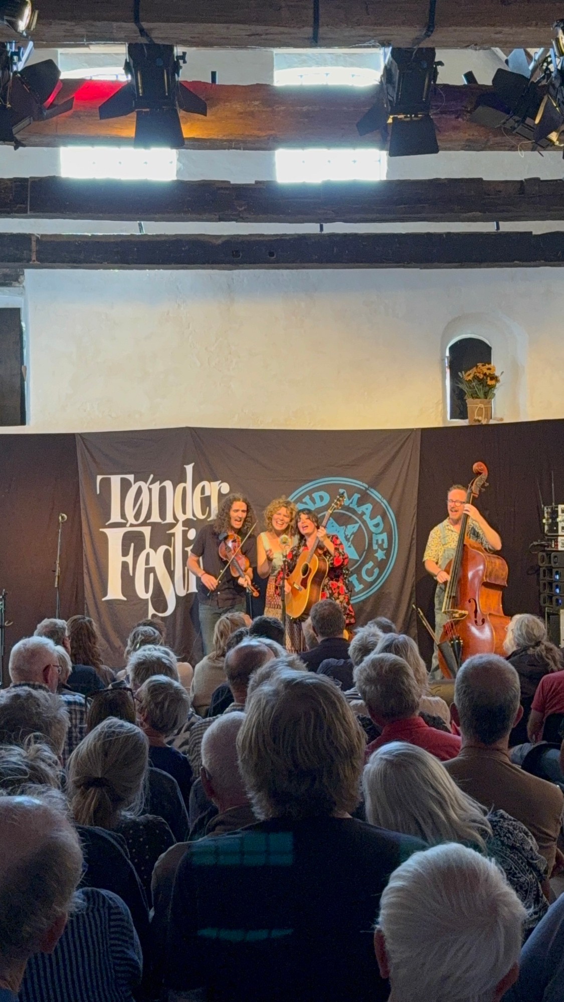 De band zingt samen rond één microfoon in een volle zaal op het Tønder Festival