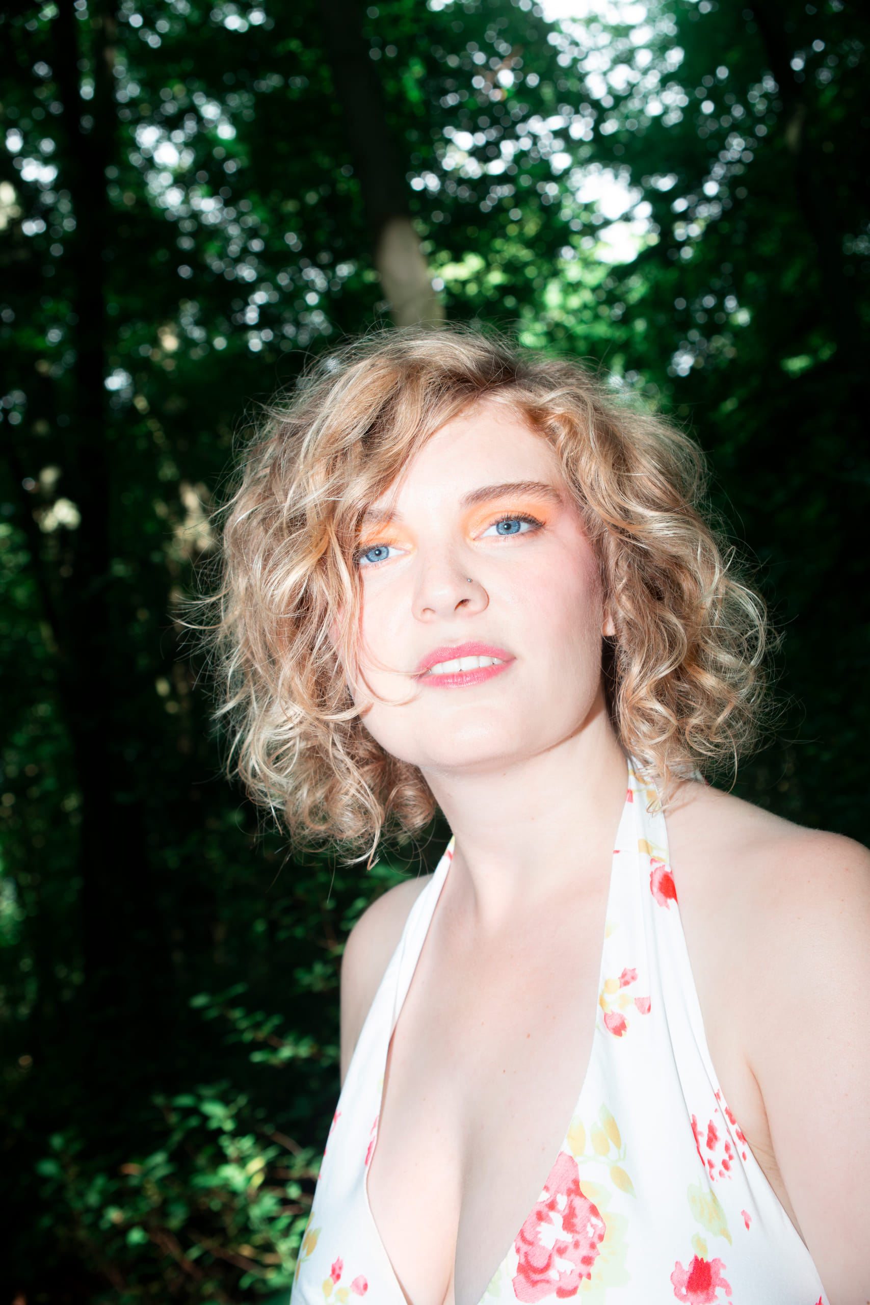 Portret van NinaLynn in het bos, met oranje oogschaduw en een bloemenjurk